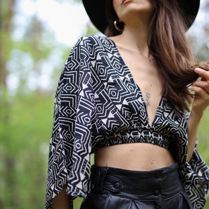 Op de afbeelding: Een vrouw draagt een zwarte hoed met brede rand, een zwart-wit geometrisch geprint crop top en een zwarte leren broek.