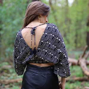 Op de afbeelding: Een zwart-wit geometrisch geprint crop top met een lage rug en een kwastband. Het top wordt gedragen met een zwarte leren broek.