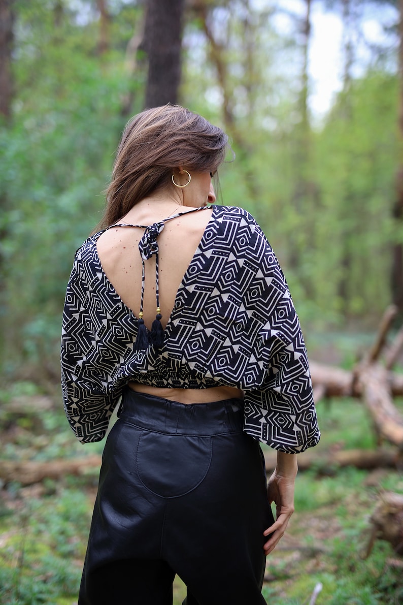 Op de afbeelding: Een zwart-wit geometrisch geprint crop top met een lage rug en een kwastband. Het top wordt gedragen met een zwarte leren broek.