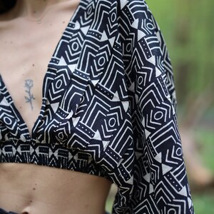 Op de afbeelding: Een zwart-wit geometrisch geprint crop top met een diepe V-hals en korte, wijde mouwen.