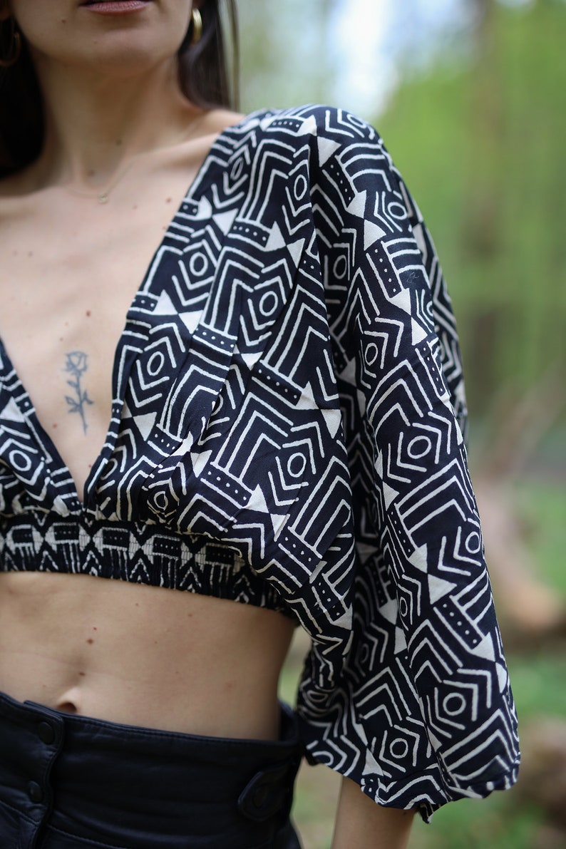 Op de afbeelding: Een zwart-wit geometrisch geprint crop top met een diepe V-hals en korte, wijde mouwen.