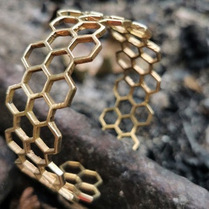 May include: A gold-toned metal bracelet with a honeycomb design. The bracelet is open and has a simple, elegant style.