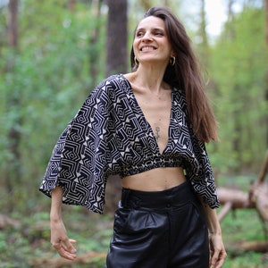 Op de afbeelding: Een vrouw draagt een zwart-wit geometrisch geprint crop top met een diepe V-hals en lange mouwen. Ze draagt ook een zwarte leren broek met een hoge taille.