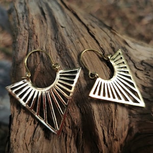 May include: A pair of gold-toned triangle-shaped earrings with a geometric design. The earrings are made of metal and have a hoop design.