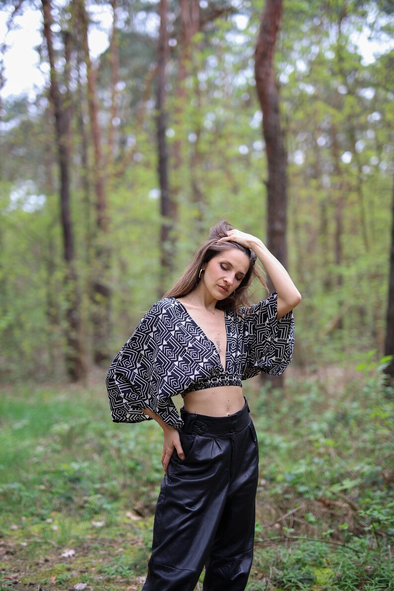 Op de afbeelding: Een vrouw draagt een zwart-wit geometrisch geprint crop top met een zwarte leren broek in een bosrijke omgeving.