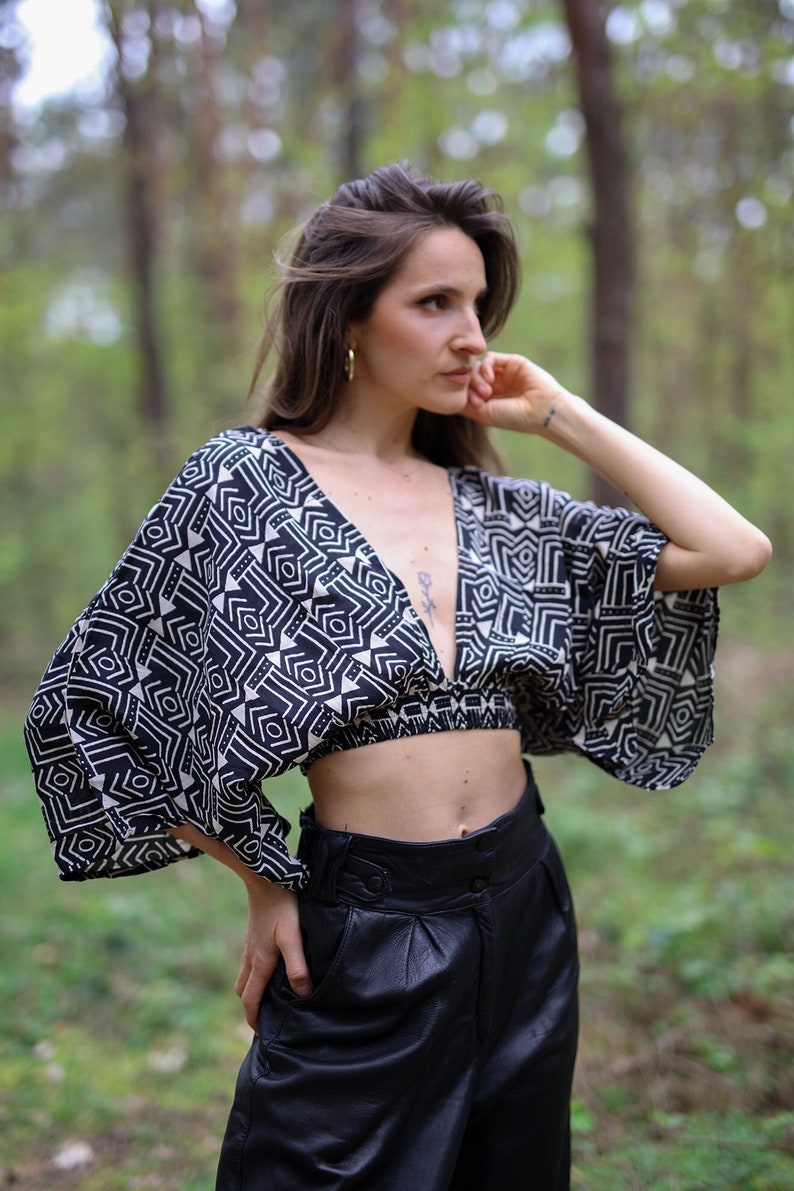 Op de afbeelding: Een vrouw draagt een zwart-wit geometrisch geprint crop top met een diepe V-hals en een zwarte leren broek.
