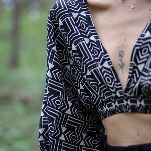 Op de afbeelding: Een zwart-wit geometrisch geprint crop top met een diepe V-hals. De top heeft een losse pasvorm en is gemaakt van een lichtgewicht stof.