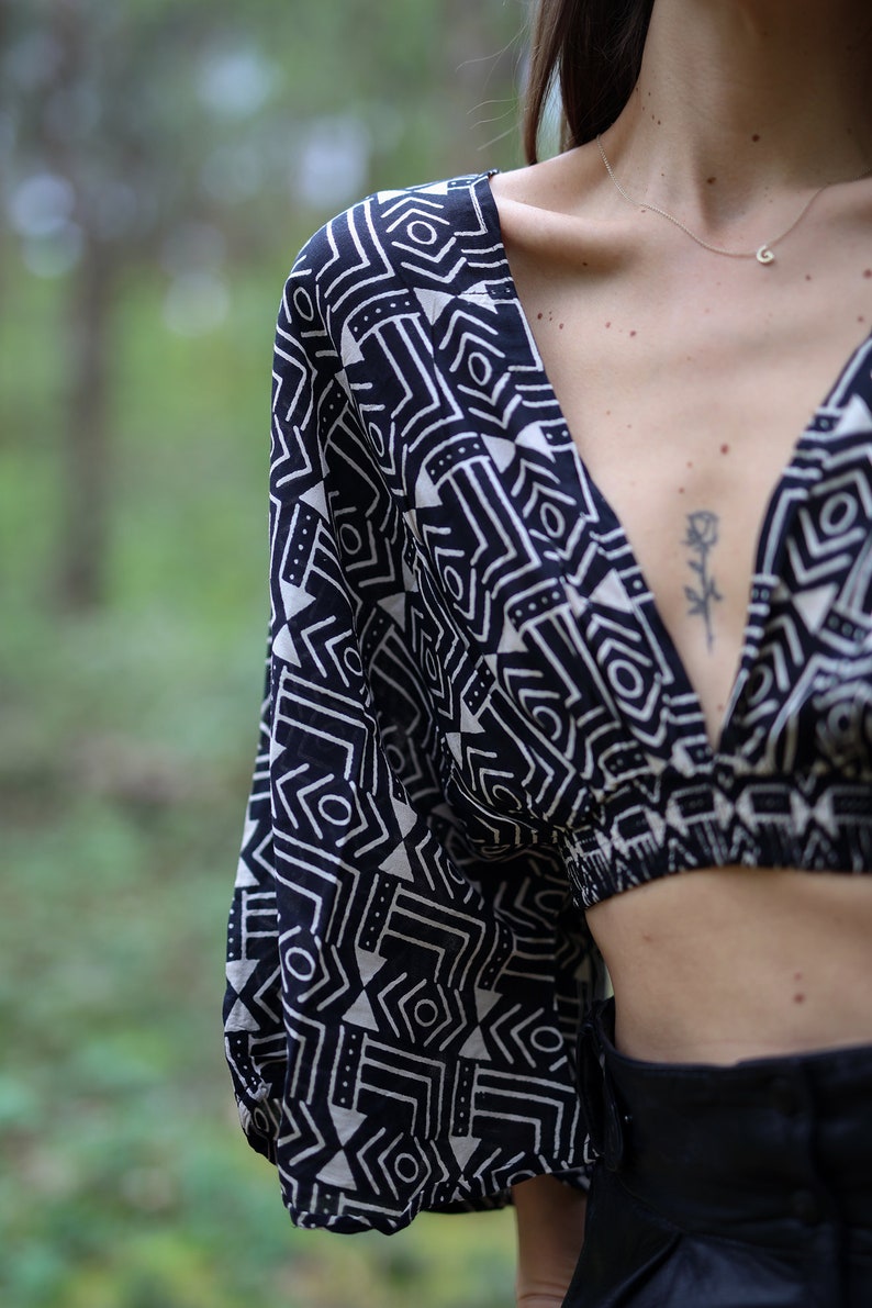 Op de afbeelding: Een zwart-wit geometrisch geprint crop top met een diepe V-hals. De top heeft een losse pasvorm en is gemaakt van een lichtgewicht stof.