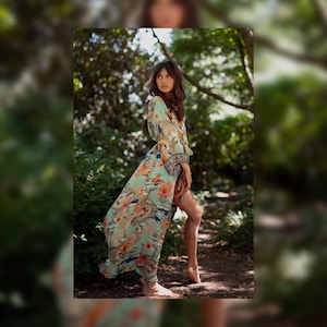 Puede incluir: Una bata larga estilo kimono de color verde claro con un estampado vibrante y multicolor de mariposas, flores y patrones circulares. La prenda tiene mangas largas y holgadas, frente abierto y un dobladillo fluido que llega hasta el suelo.