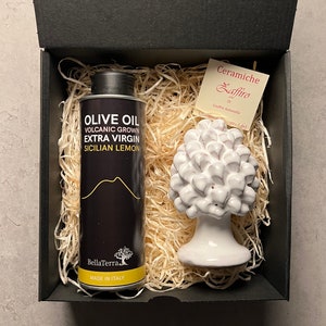 May include: A black gift box containing a white ceramic olive tree and a bottle of olive oil. The bottle is labelled "Olive Oil, Volcanic Grown, Extra Virgin, Sicilian Lemon, BellaTerra, Made in Italy". The ceramic olive tree is labelled "Ceramiche Zaffiro di Giuffre Antonella".