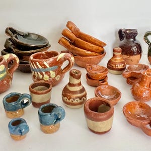May include: A collection of miniature terracotta pottery items, including mugs, pitchers, bowls, and spoons. The pieces are in various shades of brown, with some featuring blue, yellow, and green accents. The pottery has a rustic, handmade appearance.