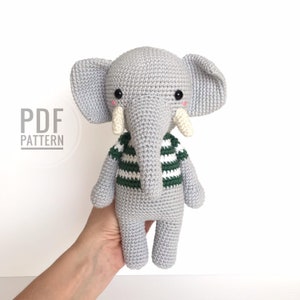 Könnte beinhalten: Ein grauer gehäkelter Elefant, der ein grün-weiß gestreiftes Hemd trägt. Der Elefant hat einen langen Rüssel und große Ohren. Der Text "PDF PATTERN" ist im Bild sichtbar.