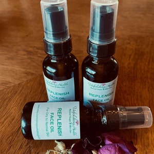 May include: Three amber glass bottles with black spray tops and white labels. The labels have green text that reads "Unfolding Health Natural Soaps & Skin Care" and "Replenish Face Oil". The label on the bottom bottle also reads "For Dry to Normal Skin".