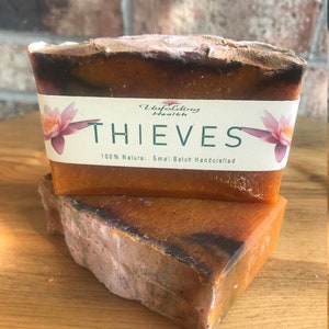 May include: Two bars of orange and brown soap with a white label that reads "Unfolding Health Thieves 100% Natural - Small Batch Handcrafted".