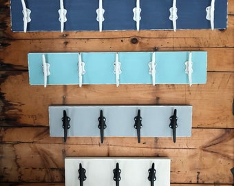 May include: Four wooden wall-mounted coat racks with different colored backgrounds and white or black cleat hooks. The top rack is blue, the second is light blue, the third is gray, and the bottom is white.