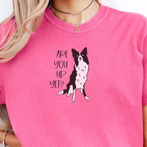 Puede incluir: Camiseta rosa brillante con una ilustraci&oacute;n en blanco y negro de un perro Border Collie. El texto "ARE YOU UP YET?" est&aacute; impreso encima del perro. La camiseta tiene mangas cortas.