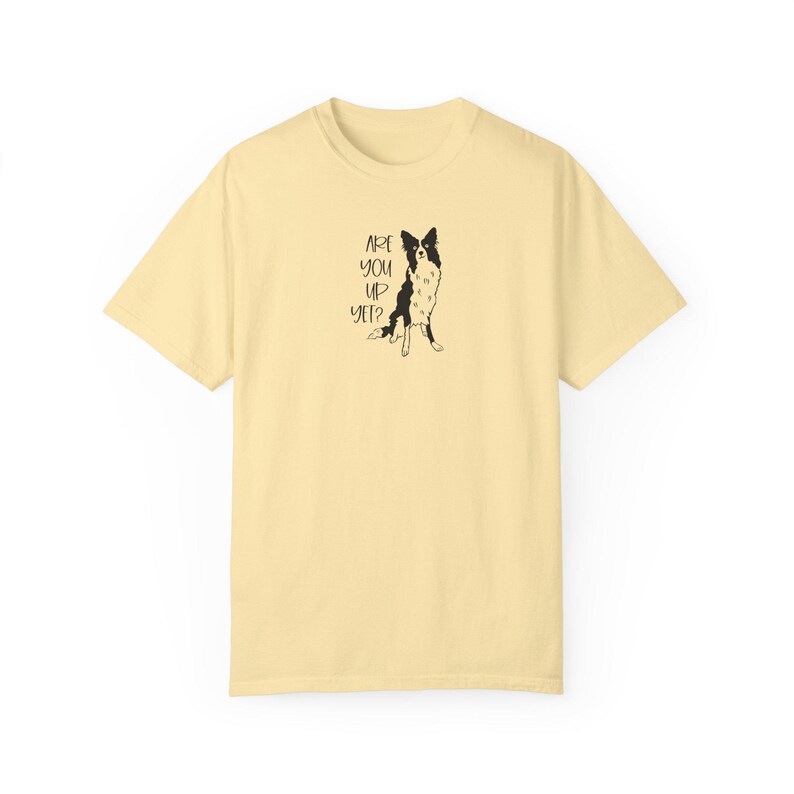 Puede incluir: Camiseta amarillo claro con una ilustraci&oacute;n en blanco y negro de un perro y el texto "ARE YOU UP YET?". El perro est&aacute; representado sentado. La camiseta tiene mangas cortas y cuello redondo.