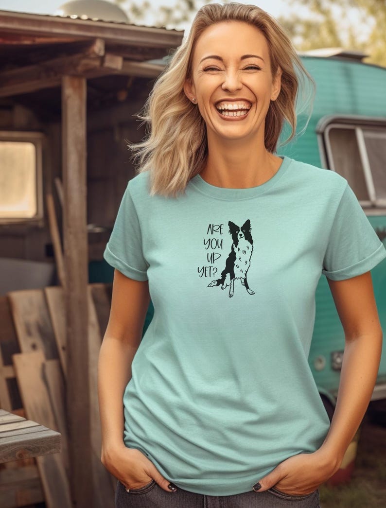 Puede incluir: Camiseta azul claro con una ilustraci&oacute;n en blanco y negro de un perro y el texto "ARE YOU UP YET?". La camiseta tiene mangas cortas y est&aacute; hecha de un material suave.