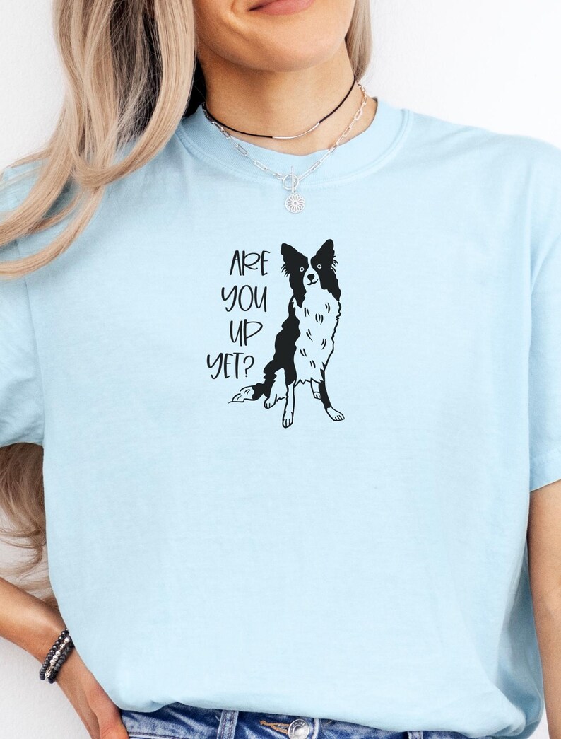 Puede incluir: Camiseta azul claro con una ilustraci&oacute;n en blanco y negro de un perro Border Collie. El texto "ARE YOU UP YET?" est&aacute; impreso en negro sobre el perro. La camiseta es de material suave.