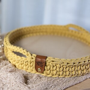 K&ouml;nnte beinhalten: Ein gelbes H&auml;keltablett mit Ledergriffen und einem "HAND MADE"-Etikett. Das Tablett befindet sich auf einer hellbraunen Oberfl&auml;che.