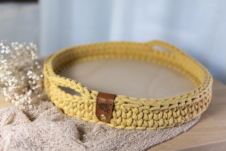 K&ouml;nnte beinhalten: Ein gelbes H&auml;keltablett mit Ledergriffen und einem "HAND MADE"-Etikett. Das Tablett befindet sich auf einer hellbraunen Oberfl&auml;che.