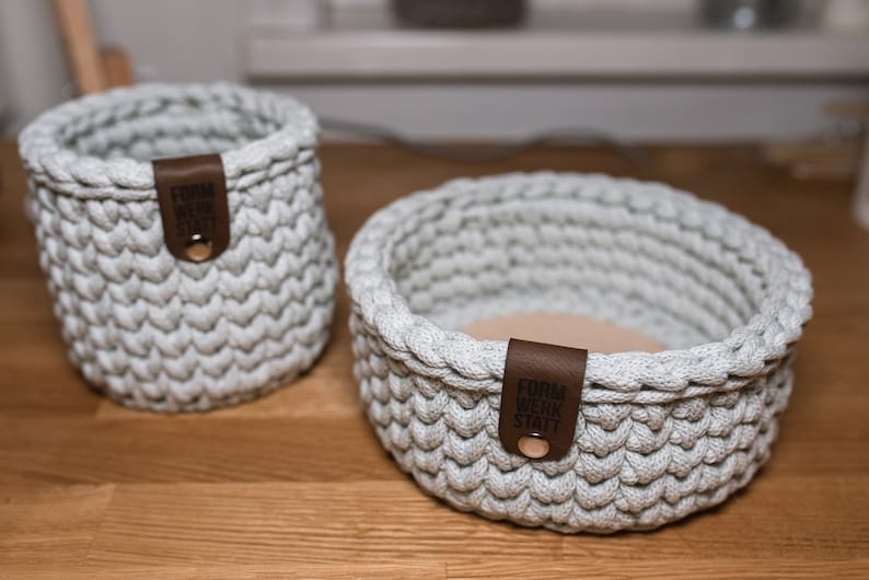 K&ouml;nnte beinhalten: Zwei graue geh&auml;kelte K&ouml;rbe mit braunen Leder-Etiketten. Der gr&ouml;&szlig;ere Korb ist rund und der kleinere Korb ist zylindrisch. Die Etiketten tragen den Text "Form Werk Statt".