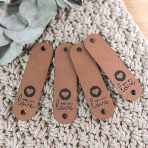 Könnte beinhalten: Vier braune Lederanhänger mit einem schwarzen Herzen und dem Text "Made with love" auf jedem Anhänger.
