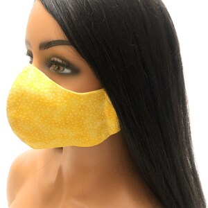 May include: A yellow face mask with a white polka dot pattern. The mask is made of fabric and has a contoured shape.