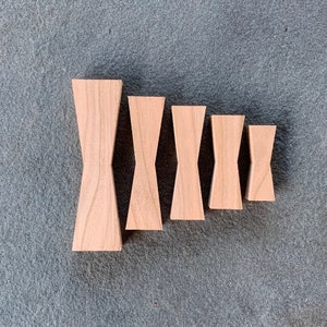 May include: Five wooden bow tie shapes in various sizes, arranged in a descending order from left to right. The bow ties are made of light brown wood and have a smooth, polished finish.