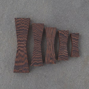 May include: Five wooden bow tie shapes in various sizes, all with a dark brown wood grain pattern.