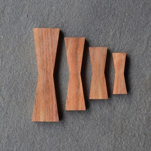 May include: Four wooden bow tie shapes in various sizes, arranged from largest to smallest. The bow ties are made of a light brown wood with a natural grain pattern.