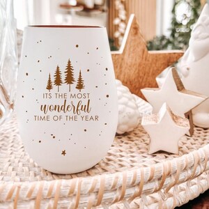 Könnte beinhalten: Weißer Kerzenhalter aus Keramik mit goldfarbenem Rand und einem winterlichen Design. Der Kerzenhalter zeigt eine Silhouette von Kiefern und den Text "Es ist die schönste Zeit des Jahres".