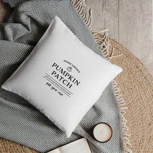 Könnte beinhalten: Ein weißes Kissen mit schwarzem Text, der "Home Grown Pumpkin Patch Apples Hayrides Corn Maze Pick Your Own" lautet. Das Kissen liegt auf einer grauen und weißen Decke und einem braunen gewebten Teppich.