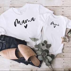May include: White t-shirt with the word "mama" in black script with a small heart underneath. A white baby onesie with the word "mini" in black script with a small heart underneath.