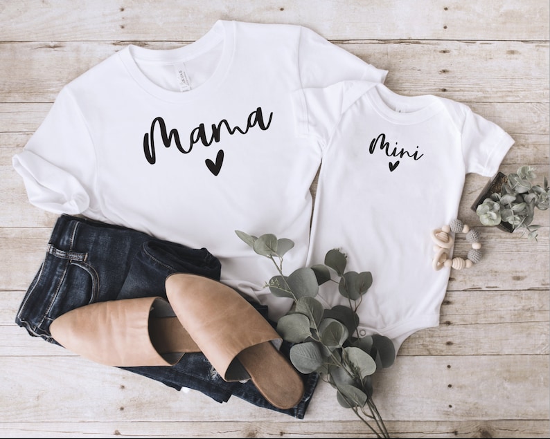 May include: White t-shirt with the word "mama" in black script with a small heart underneath. A white baby onesie with the word "mini" in black script with a small heart underneath.