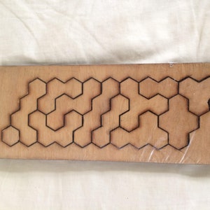 May include: A wooden board with a honeycomb pattern cut out. The board is light brown and the honeycomb pattern is dark brown.