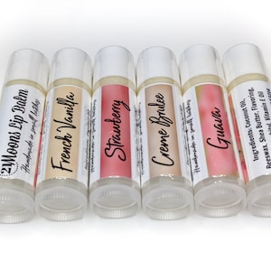 May include: Six clear lip balm tubes with colorful labels. The labels have the following text: 2Moons Lip Balm, French Vanilla, Strawberry, Creme Brulee, Guava. The ingredients are listed on the last tube: Coconut Oil, Beeswax, Shea Butter, Flavoring, Liquid Sorbitol, Vitamin E Oil.