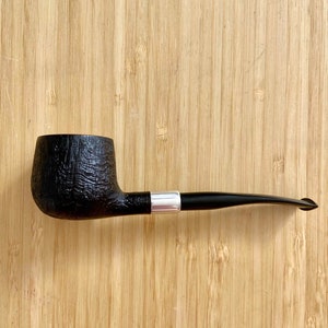 May include: A black briar smoking pipe with a silver band on the stem. The pipe is on a wooden surface.