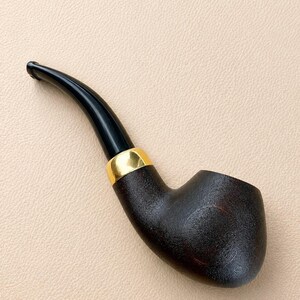 May include: A tobacco pipe featuring a dark brown, textured bowl and a smooth, curved black stem. The pipe is accented with a polished gold-colored metal band connecting the bowl to the stem, creating a distinct contrast between the materials.