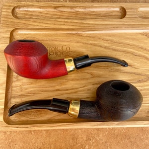 May include: Two wooden smoking pipes on a wooden tray. One pipe is red and the other is black.