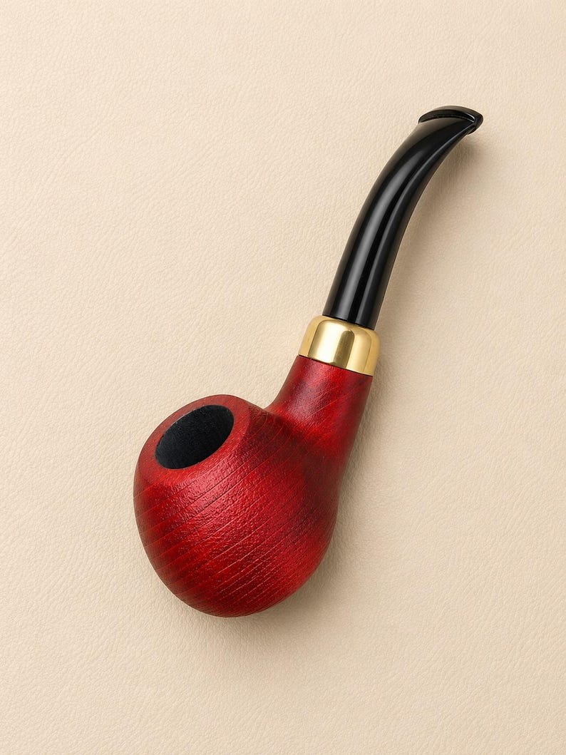 May include: A tobacco pipe featuring a deep red wooden bowl with a visible grain texture, a polished gold-colored metal band connecting the bowl to the stem, and a smooth, curved black acrylic mouthpiece extending from the top of the pipe.