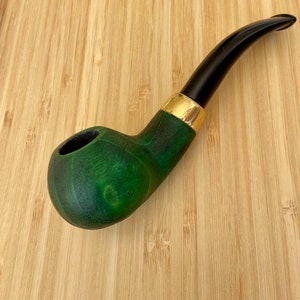May include: A green wooden pipe with a black stem and a gold band. The pipe is on a wooden surface.