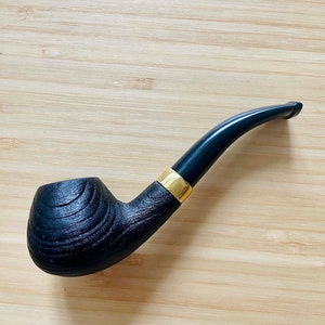 May include: A black smoking pipe with a curved stem and a textured bowl. The pipe has a gold-colored band where the stem meets the bowl. The bowl has a wood-grain texture.