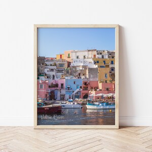 May include: A colorful cityscape with pastel-colored buildings lining a harbor. Boats are docked in the water, and the sky is a bright blue.
