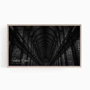 May include: Black and white photograph of a library interior with high vaulted ceilings and rows of bookshelves. The image is framed in a light wood frame.