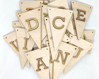 Op de afbeelding: Een set houten driehoekige vlaggen met letters van het alfabet, waaronder A, C, D, E, I, J, N en V. De vlaggen zijn gemaakt van lichtbruin hout en hebben gaten om aan elkaar te rijgen.