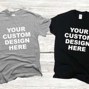 May include: Two t-shirts, one gray and one black, with the text "YOUR CUSTOM DESIGN HERE" printed in white on the front.