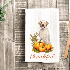 May include: White kitchen towel with a yellow Labrador Retriever sitting in front of three orange pumpkins and a bunch of wheat. The text "Thankful" is printed in orange at the bottom of the towel.