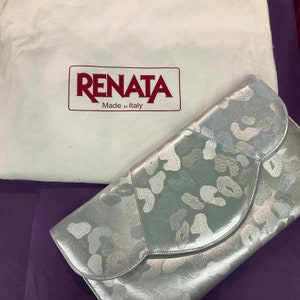May include: A silver clutch purse with a white floral pattern. The purse has a flap closure and is made in Italy. The brand name "RENATA" is printed in red on a white dust bag.
