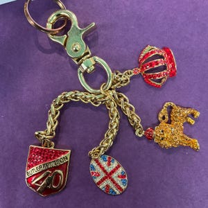 May include: A gold key chain with a red, white, and blue Union Jack charm, a gold lion charm, a red crown charm, and a red shield charm with the text "BUTLER & WILSON 40" in gold.